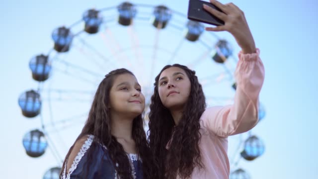 Zwei-schöne-Freundinnen-machen-eine-Selfie-im-Hintergrund-von-einem-Riesenrad.-4-K.-Nahaufnahme