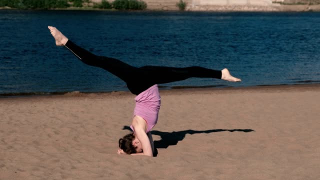 Frau-beim-Yoga-am-Strand-am-Fluss-in-der-Stadt.-Schöne-Aussicht.-Handstand.-Schnur-in-der-Luft.-High-Speed.