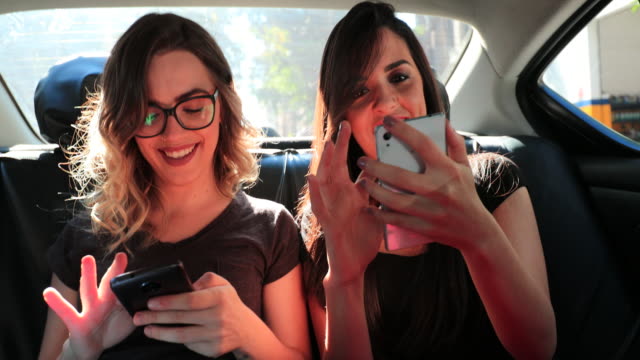 Zwei-Mädchen-auf-dem-Rücksitz-eines-Autos-prüfen-Handy-zusammen.-Freundinnen-Surfen-auf-ihrem-Smartphone-während-der-Fahrt-mit-Taxi