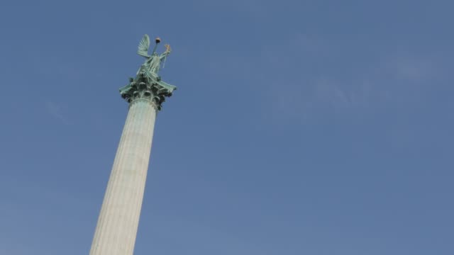 The-Millennium-Monument-on-Heroes-square-and-Hungarian-capital-city-of-Budapest-tilting-4K-2160p-UltraHD-footage---Hosok-ter-statues-by-the-day-in-front-of-blue-sky-4K-3840X2160-UHD-tilt-video