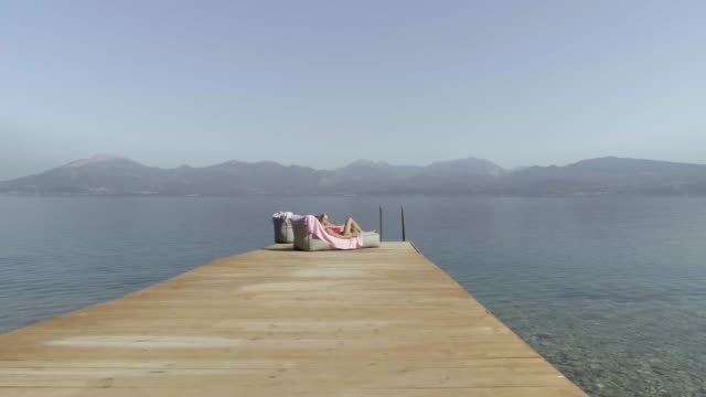 Vista-aérea-pasando-por-dos-atractiva-mujer-tomando-el-sol-en-Panagopoula,-Grecia.