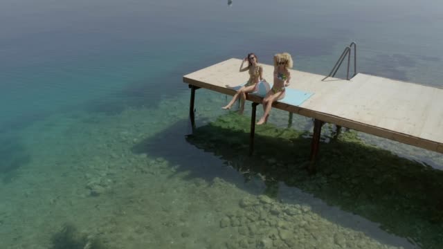Vista-aérea-de-dos-mujeres-se-sienta-en-la-cubierta-de-madera-en-Panagopoula,-Grecia.