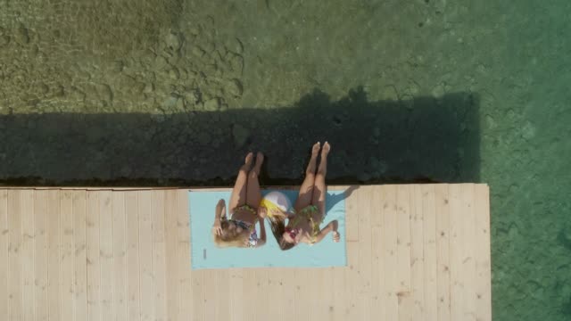 Aerial-view-of-two-women-sits-on-wooden-deck-in-Panagopoula,-Greece.