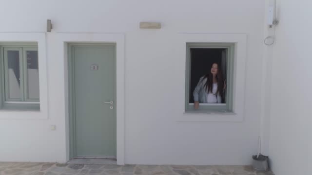 Vista-aérea-de-la-ventana-de-apertura-de-la-mujer-en-casas-blancas-tradicionales,-Grecia.