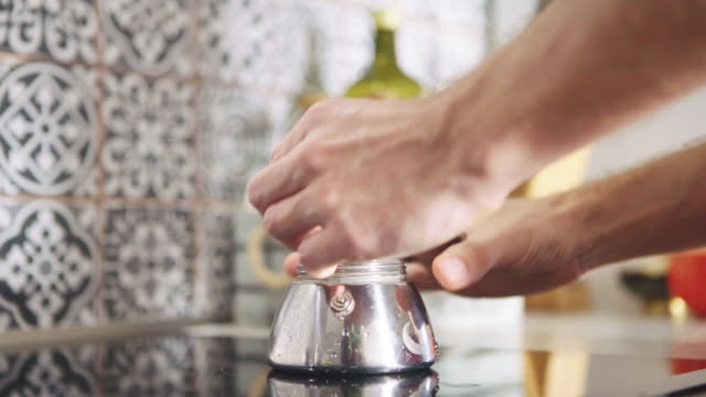 Morning-coffee-preparation.-Video-of-man's-hands-putting-mokka-coffee-maker-pot-on-modern-glass-kitchen-stove-top.-Food-preparation-in-modern-kitchen-concept-4K-footage.