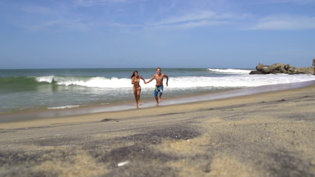 SLOW-MOTION:-Smiling-couple-running-along-the-sunny-beach