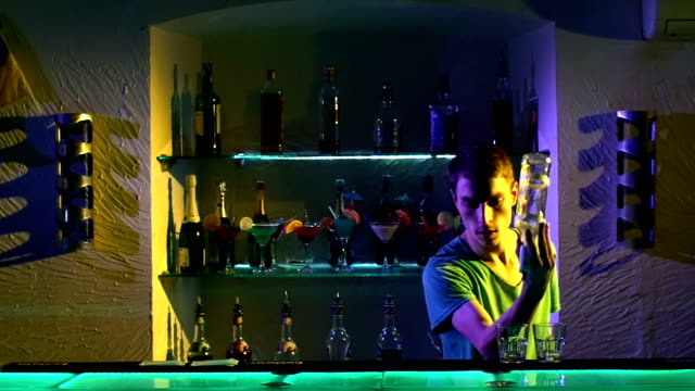 Young-barman-making-tricks-with-two-glasses-and-bottle--standing-behind-the-bar,-catching,-throwing-up,-cocktail,-slow-motion