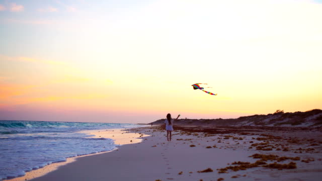 Little-running-girl-with-flying-kite-on-tropical-beach-at-sunset.-Kids-play-on-ocean-shore.-Child-with-beach-toys.