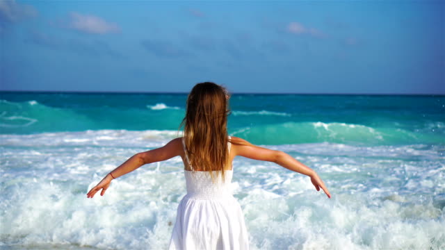 Liebenswert-glückliches-kleines-Mädchen-auf-weißen-Strand-mit-Blick-auf-den-Ozean.-Laut-Meer-und-einem-kleinen-niedlichen-Kind