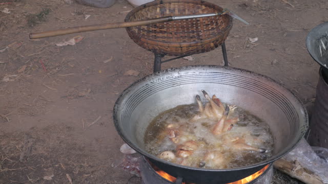 Deep-frying-chickens-in-a-large-wok-cooking-on-a-charcoal-and-wood-brazier-stove-outdoors
