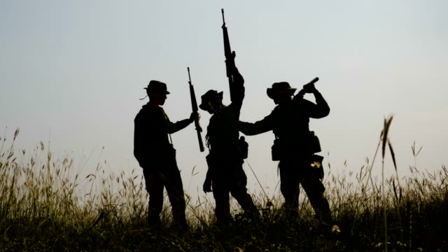 Silueta-de-tres-completamente-equipados-y-armados-soldados-de-pie-en-el-campo-de-batalla-después-de-la-guerra.