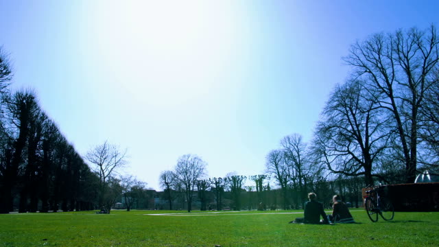 Cielo-azul-sobre-verde-parque,-pareja-descansando-fuera-de-fin-de-semana,-tranquilidad