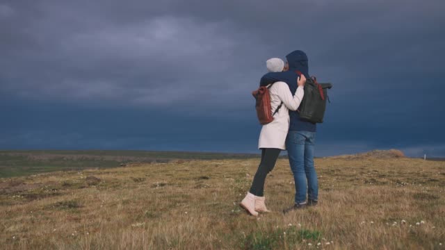 Young-loving-couple-hugging-in-field-on-background-of-epic-dramatic-clouds,-slow-motion
