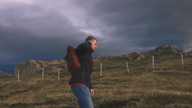 Young-man-walking-in-field-way-to-mountains-with-dramatic-sky-background,-slow-motion