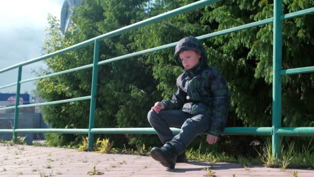 Sieben-Jahr-Alter-Junge-sitzt-auf-einem-Zaun-in-den-Park-und-schaut-sich-um.