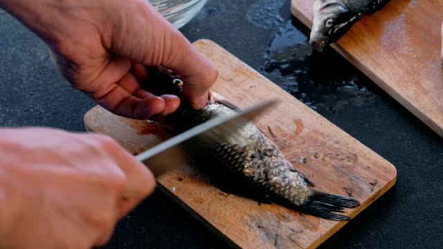 Man-cleans-carp-from-the-scales-on-wooden-board.-Close-up-hands.-Cooking-a-fish