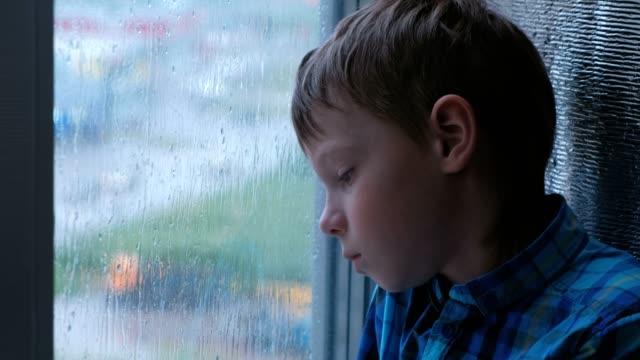 Junge-schaut-aus-dem-Fenster-im-Regen-und-ist-traurig.
