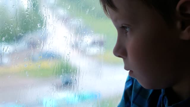 Junge-schaut-aus-dem-Fenster-im-Regen-und-ist-traurig.
