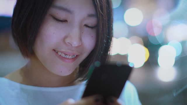 Porträt-der-attraktiven-japanischen-Mädchen-tragen-legere-Kleidung-nutzt-Smartphone.-Im-Hintergrund-Plakate-Großstadt-Werbung-Lichter-leuchten-in-der-Nacht.