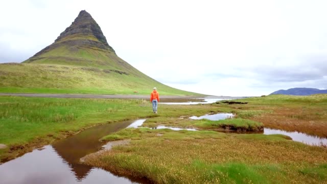 Drone-aerial-view-of-Caucasian-female-at-Kirkjufell-mountain-contemplating-nature.-Shot-in-West-Iceland,-Springtime.-People-travel-carefree-lifestyles-concept--4K-video