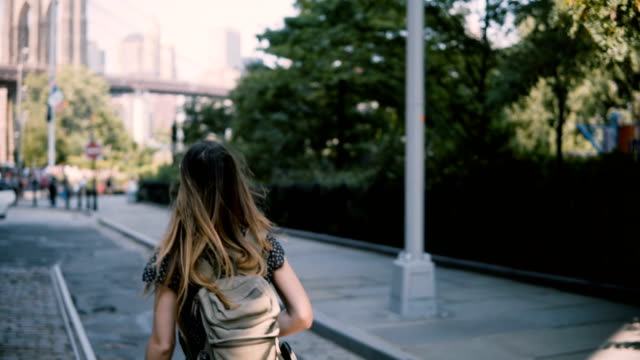 Kamera-folgt-junge-aufgeregt-weibliche-Touristen-mit-Rucksack-in-Sonnenbrille-genießen-Sie-New-York-City-Straßen,-lächelt-glücklich-4K