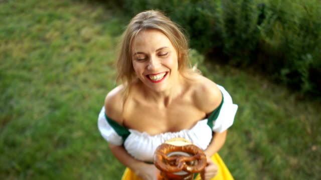 Festival-Oktoberfest.-A-woman-in-a-Bavarian-suit-with-a-large-glass-of-beer-and-a-pretzel-in-her-hands-laughs-cheerfully-and-looks-into-the-camera.-Top-View