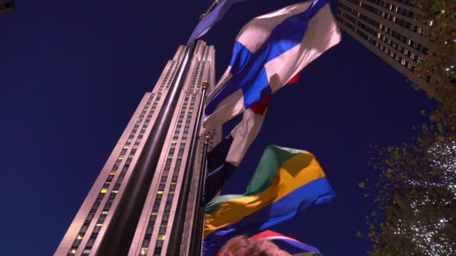 Video-von-einige-Fahnen-durch-den-Wind-in-den-Vordergrund-und-die-Rockefeller-Gebäude-im-Hintergrund-in-Manhattan,-New-York-zog.