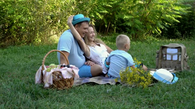 La-familia-tenía-un-picnic-en-la-naturaleza.-Mamá,-papá-y-pequeño-hijo-divirtiéndose-y-jugando-con-los-sombreros-en-la-hierba-en-el-parque.