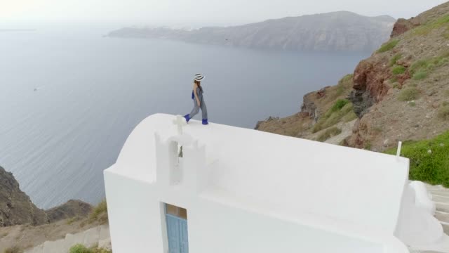 Vista-aérea-mujer-caminando-en-el-techo-de-la-casa-tradicional-de-Santorini,-Grecia.