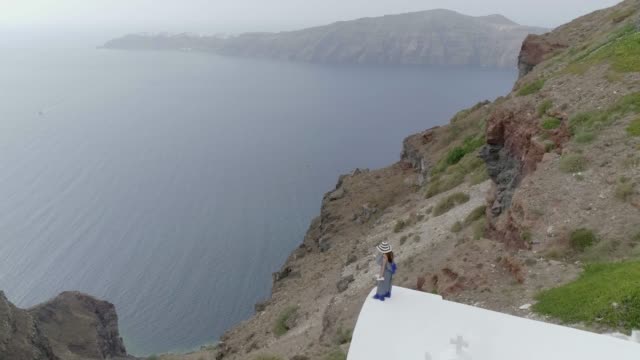 Aerial-view-woman-standing-in-the-edge-of-roof-on-Santorini-traditional-house.