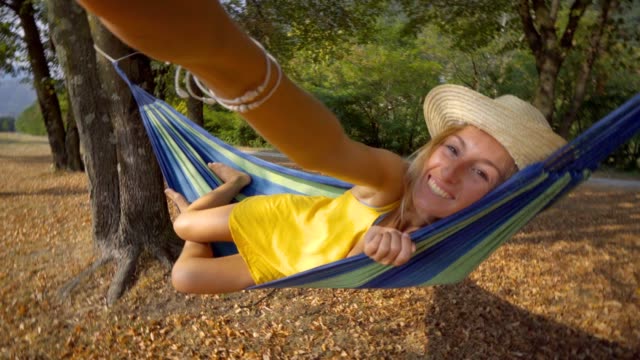 Young-woman-taking-selfie-on-hammock-relaxing-at-sunset-in-Autumn--People-travel-vacations-technology-communication-concept