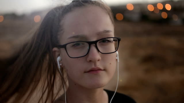 Teenage-girl-with-eyeglasses-listening-to-the-music-on-sunset,-close-up