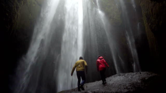 Junge-Brautpaar-stehend-unter-wunderschönen-Wasserfall-Gljufrabui-in-Island-und-hebt-die-Hände,-Gefühl-von-Freiheit-und-Freude