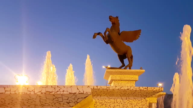 Korinth,-Griechenland,-5.-Oktober-2017.-Nachtstunde-des-Pegasus-Statue-in-Korinth-in-Griechenland-gegen-den-Brunnen.-Eine-schöne-Szene.