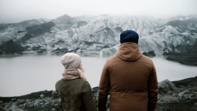 Back-view-of-young-couple-standing-in-Ice-lagoon.-Traveling-man-and-woman-exploring-the-Iceland-together