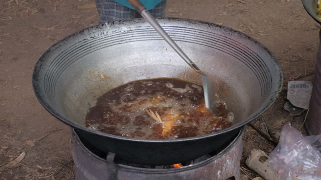 Rühren-braten-Fisch-in-einem-großen-Outdoor-Wok-Kochen-über-behelfsmäßigen-Feuerstelle-(Nahaufnahme)