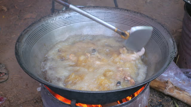 Stir-frying-chickens-in-a-large-wok-cooking-on-a-charcoal-and-wood-brazier-stove-outdoors