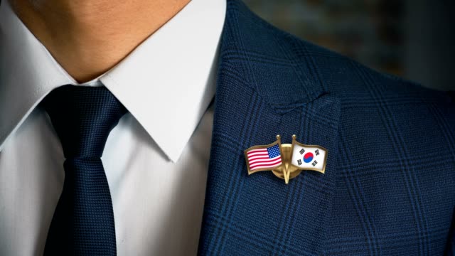 Businessman-Walking-Towards-Camera-With-Friend-Country-Flags-Pin-United-States-of-America---South-Korea