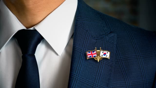 Businessman-Walking-Towards-Camera-With-Friend-Country-Flags-Pin-United-Kingdom---South-Korea