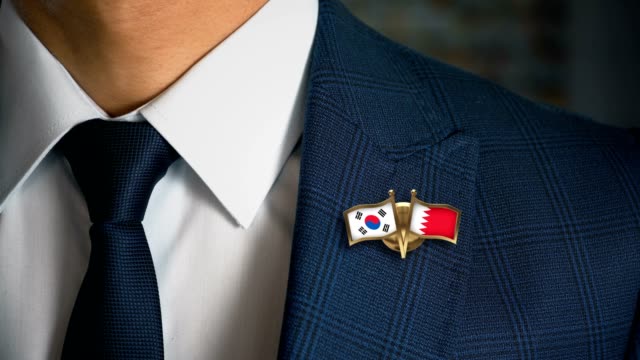 Businessman-Walking-Towards-Camera-With-Friend-Country-Flags-Pin-South-Korea---Bahrain