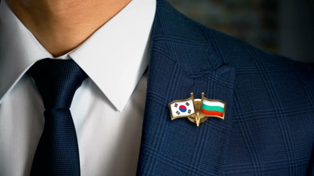 Geschäftsmann-zu-Fuß-in-Richtung-Kamera-mit-Freund-Land-Flaggen-Pin-Südkorea---Bulgarien