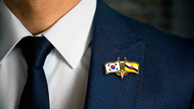 Businessman-Walking-Towards-Camera-With-Friend-Country-Flags-Pin-South-Korea---Brunei