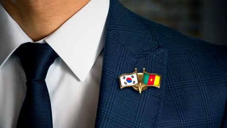 Businessman-Walking-Towards-Camera-With-Friend-Country-Flags-Pin-South-Korea---Cameroon