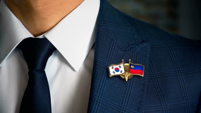 Empresario-caminando-hacia-cámara-con-amigo-país-banderas-Pin-Corea-del-sur---Liechtenstein