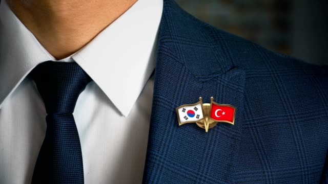Geschäftsmann-zu-Fuß-in-Richtung-Kamera-mit-Freund-Land-Flaggen-Pin-Südkorea---Türkei
