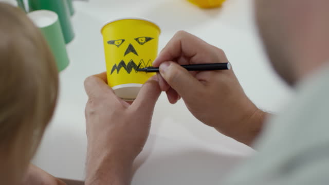 Man-Drawing-Spooky-Face-on-Halloween-Cup