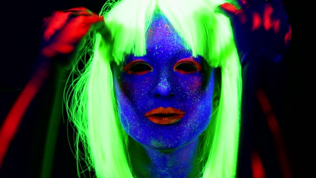 Woman-with-UV-face-paint,-wig,-glowing-clothing-dancing-in-front-of-camera,-face-close-up-of-make-up.-Caucasian-woman.-.