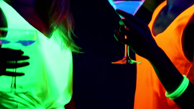 Frauen-mit-UV-face-Farbe,-leuchtende-Armbänder,-Getränke,-leuchtende-Kleidung-tanzen-gemeinsam-vor-der-Kamera,-Nahaufnahme-von-Getränken.-Kaukasischen-und-asiatischen-Frau.-.