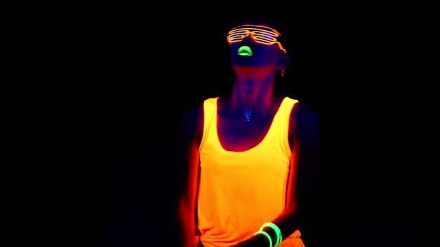 Woman-with-UV-face-paint,-glowing-clothing,-glowing-glasses,-bracelet-dancing-in-front-of-camera,-half-body-shot.-Asian-woman.-.