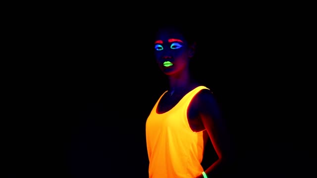 Woman-with-UV-face-paint,-glowing-clothing,-glowing-bracelet-in-front-of-camera,-half-body-shot.-Asian-woman.-.